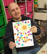 Service user John holding a sunflower created with tissue mosaics on canvas